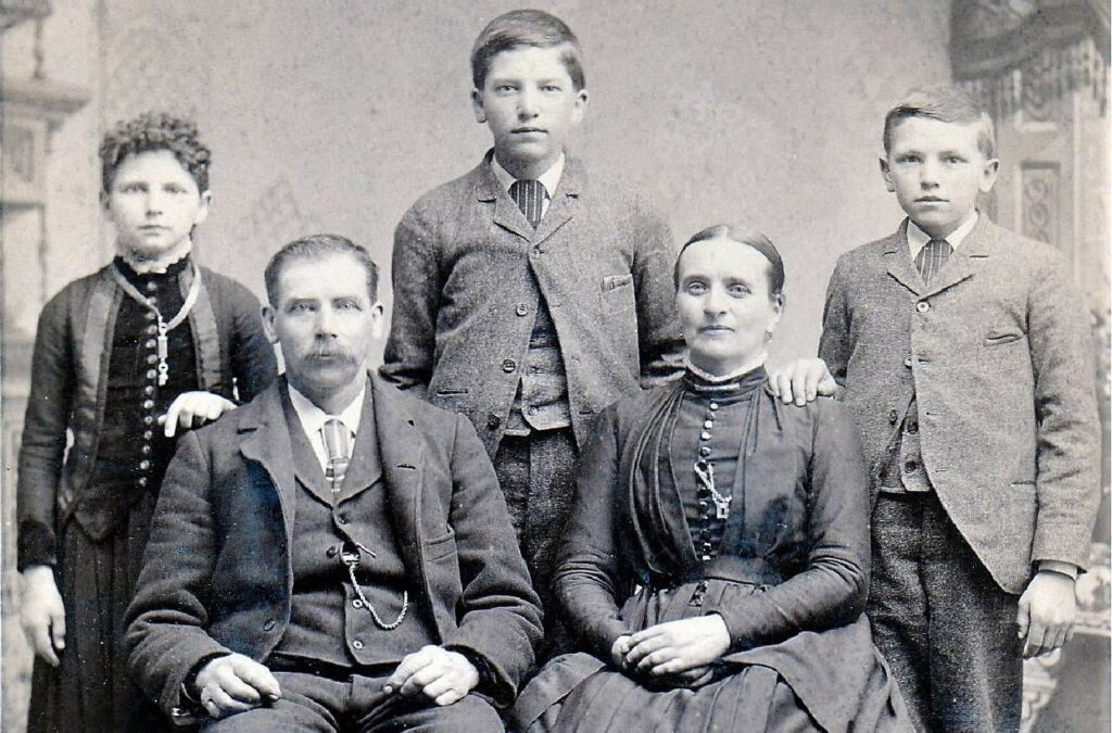 genealogy family photo with mum, dad, and three children standing behind the parents who are sat