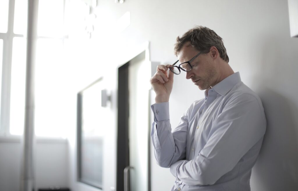 man with glasses leaning against a wall