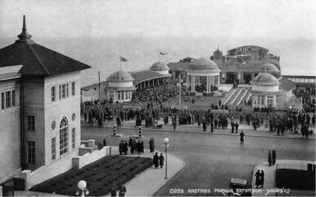 Black and white image of a pier, with a hotel on the left.