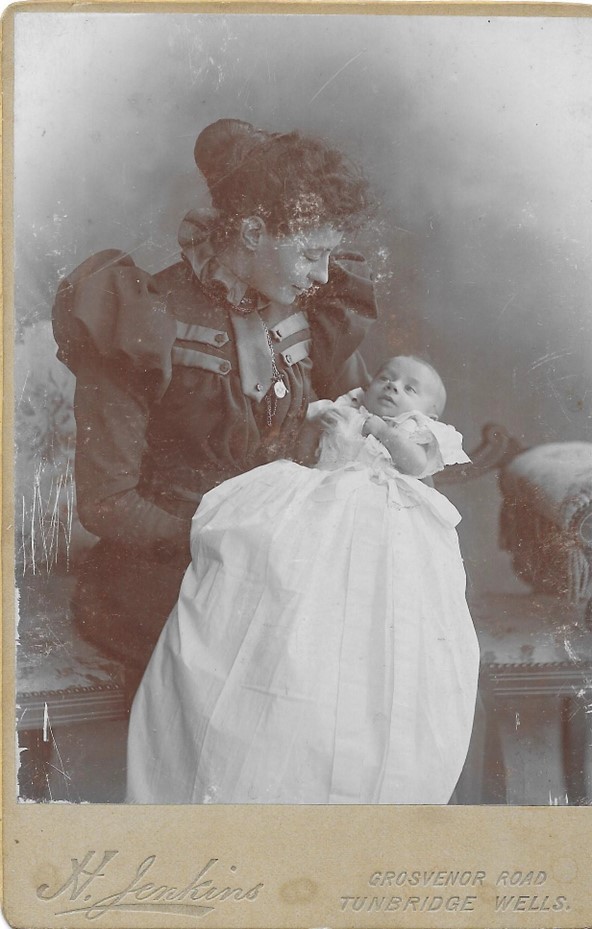 Black and white image of a woman sat down holding a baby in a baptism gown.